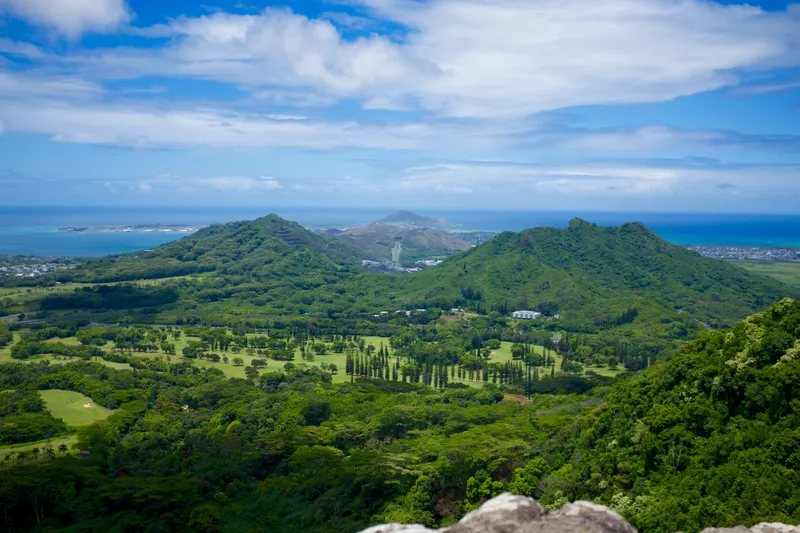 Lush green Koolau mountain ridges and valleys stretching toward the ocean under scattered clouds