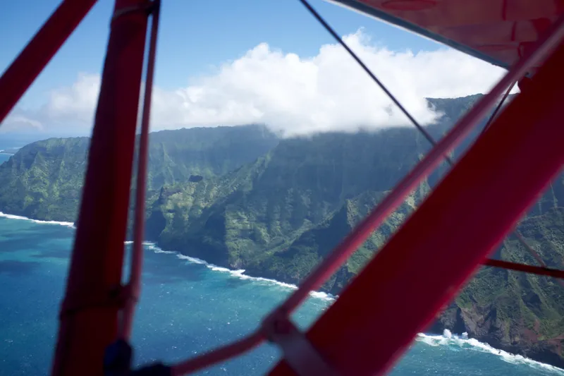 Na Pali Coast sea cliffs and turquoise water seen through the struts of a red biplane