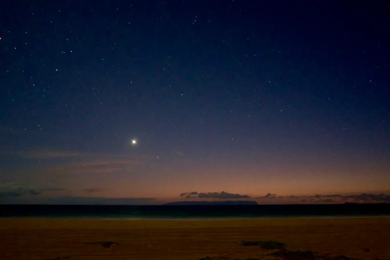 Starry night sky with a bright planet glowing above the ocean horizon at a Hawaiian beach