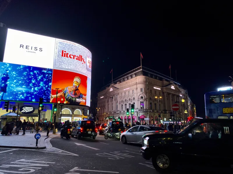 Piccadilly Circus at night with glowing billboard screens, black cabs, and bustling traffic