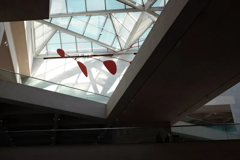 Red Calder mobile suspended beneath a glass skylight inside a modern museum atrium