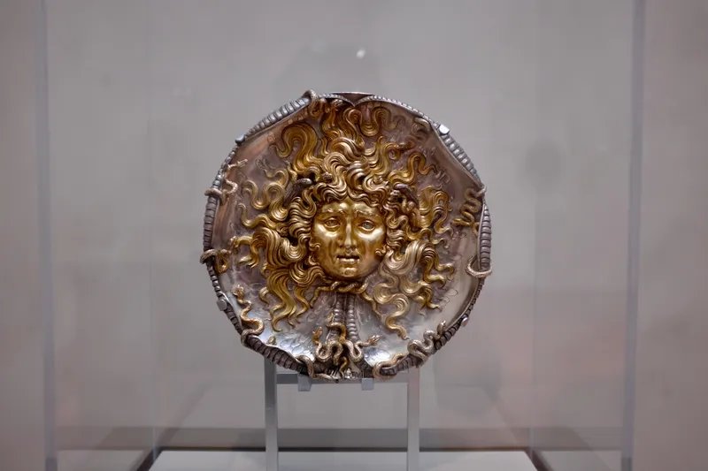 Gilt silver Medusa shield with writhing snake hair displayed in a museum case