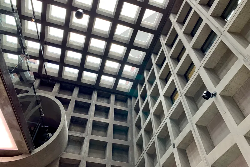 Concrete coffered ceiling with square skylights and a circular stairwell inside a brutalist museum
