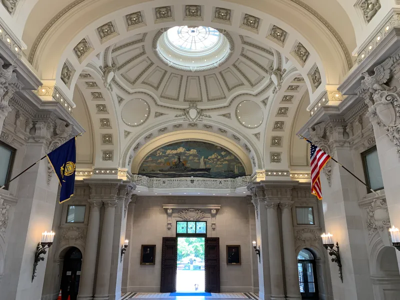 Ornate domed rotunda inside Bancroft Hall with a naval mural, American flag, and Corinthian columns