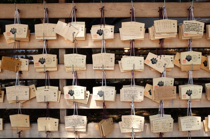 Wooden ema prayer tablets hanging on racks at a Japanese shrine, covered in handwritten wishes