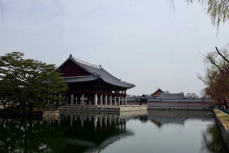Gyeonghoeru banquet hall reflected in its surrounding pond with pine trees and willow branches framing the scene