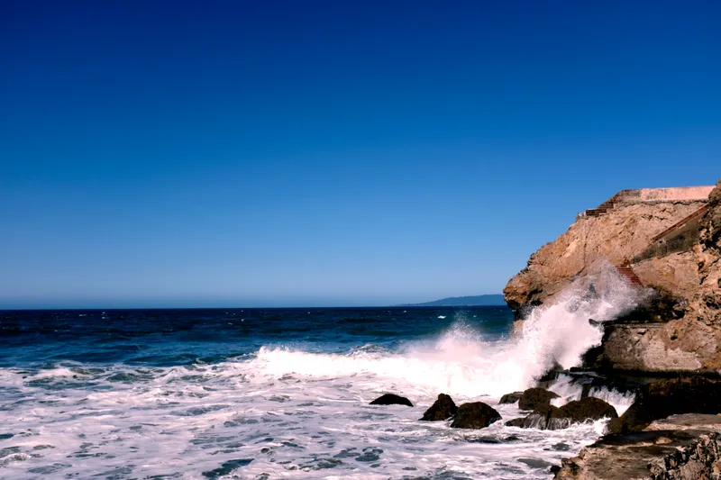 Waves crashing against rocky cliffs under a deep blue sky on the Northern California coast