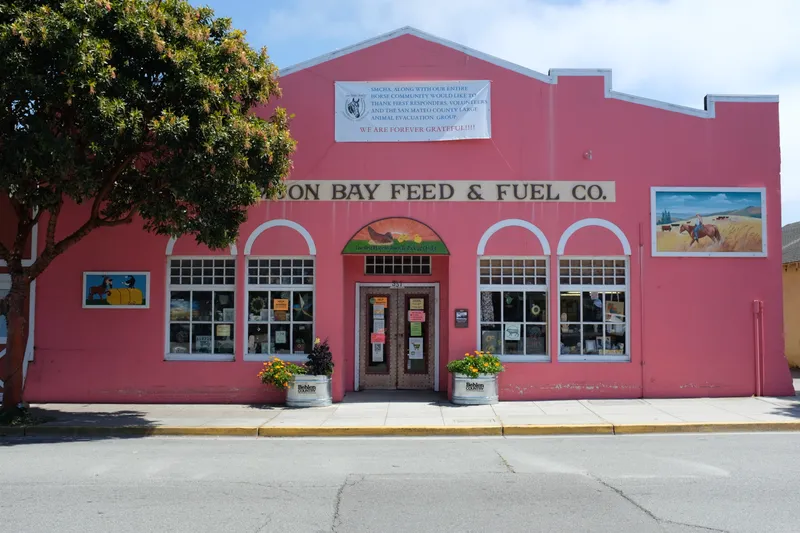 Pink facade of Half Moon Bay Feed and Fuel Co. storefront with arched windows and flower planters