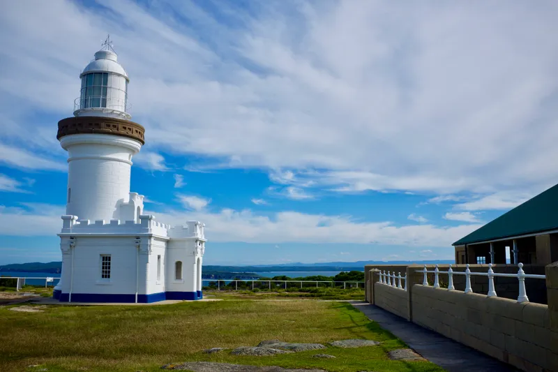 White Byron Bay lighthouse standing on a grassy headland under bright blue sky with scattered clouds