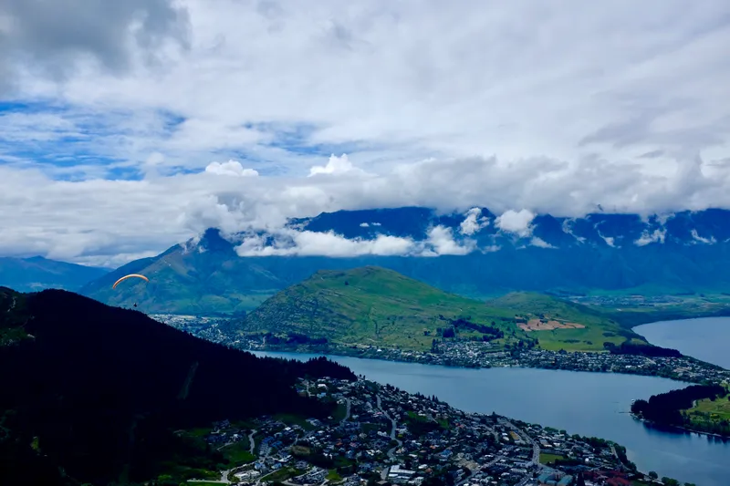 Paraglider soaring over Queenstown, Lake Wakatipu, and cloud-wrapped Remarkables mountains
