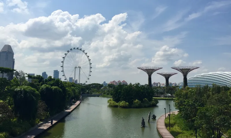 Singapore Flyer and Supertree Grove across a waterway at Gardens by the Bay under billowing clouds