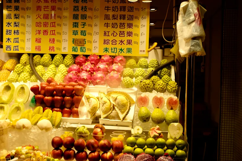 Tropical fruit stand at a Taiwanese night market displaying durian, dragon fruit, and guava with Chinese price signs