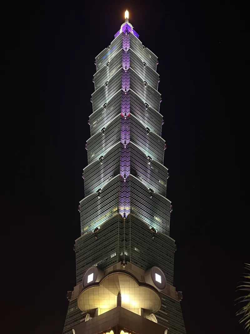 Taipei 101 tower illuminated with purple lights against the night sky, viewed from below